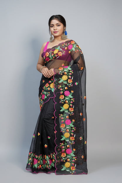 Woman in a traditional saree with colorful patterns standing against a dark wall with decorative items.