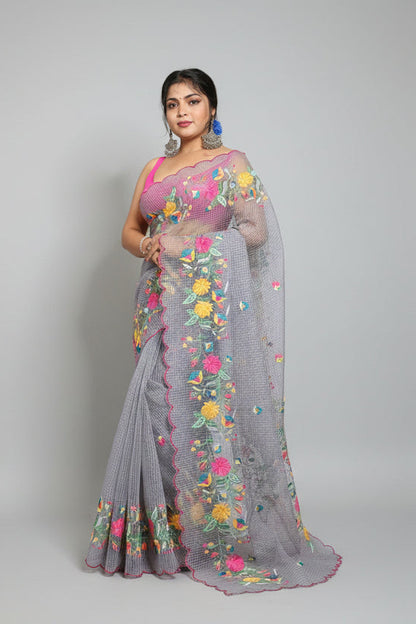 Woman in a saree with floral patterns standing next to traditional pots against a dark background.